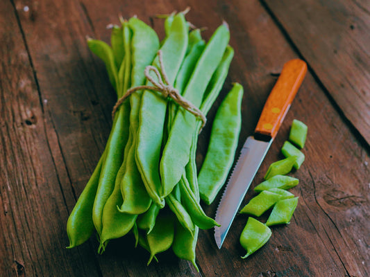 A bunch of fresh green beans and a knife are placed on a wooden surface.