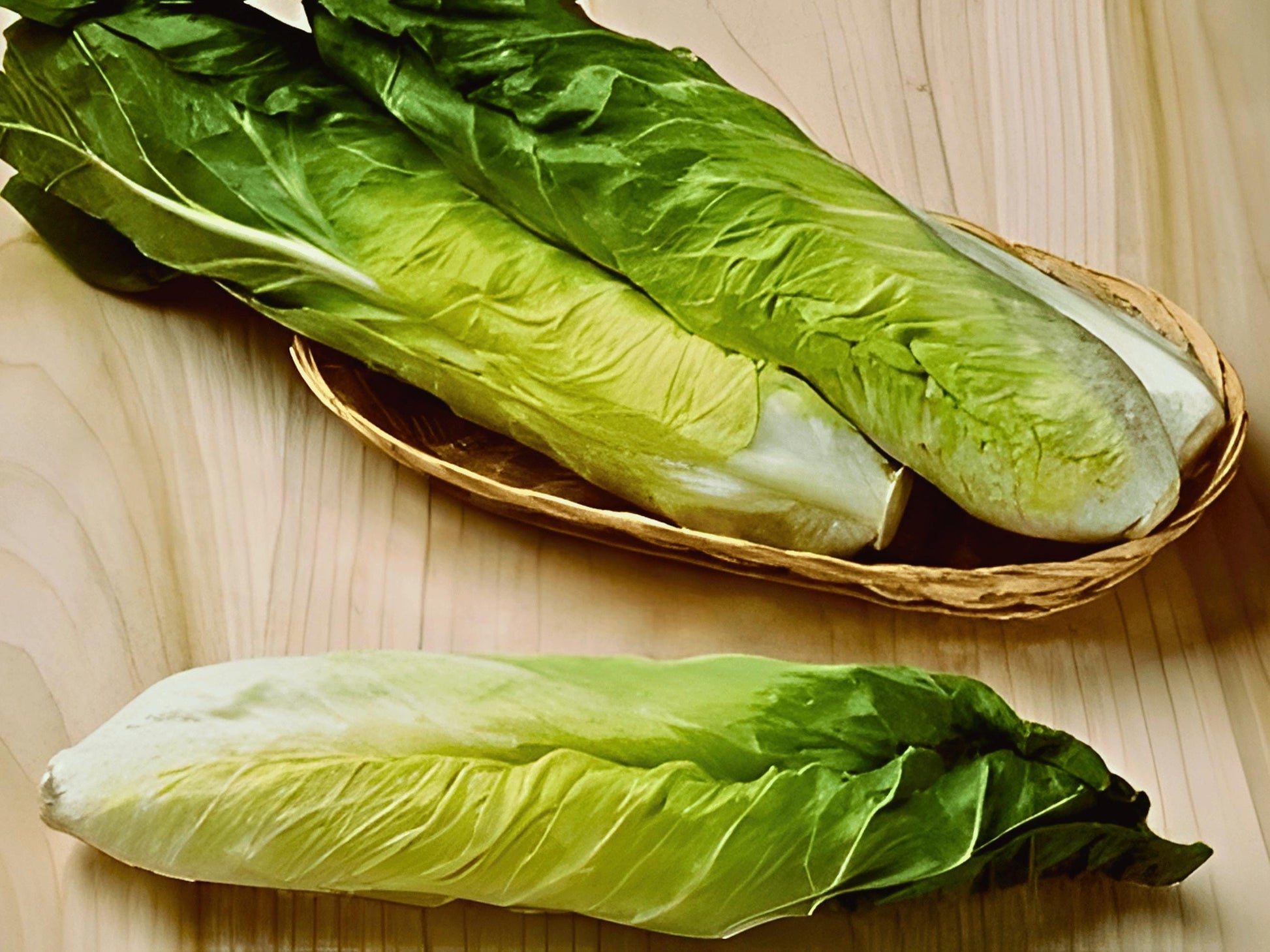 a pair of fresh green lettuce leaves, one in a woven basket and the other on a wooden surface.