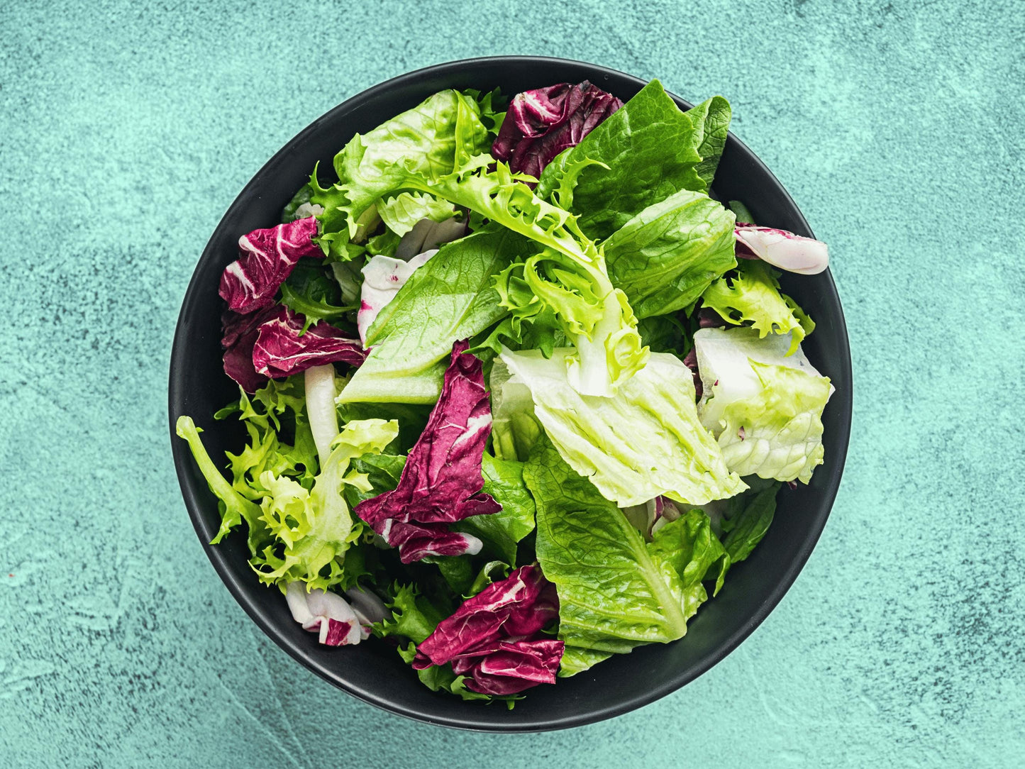 A bowl filled with a fresh salad of various green and purple lettuce leaves.