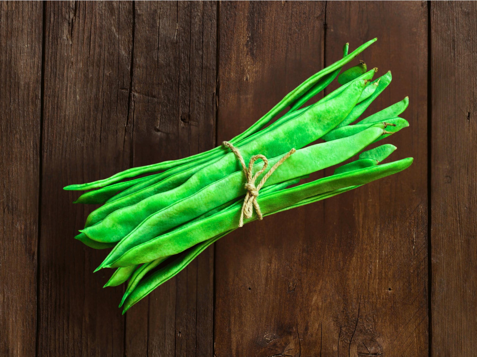 A bundle of fresh green beans tied with a string, resting on a wooden surface.
