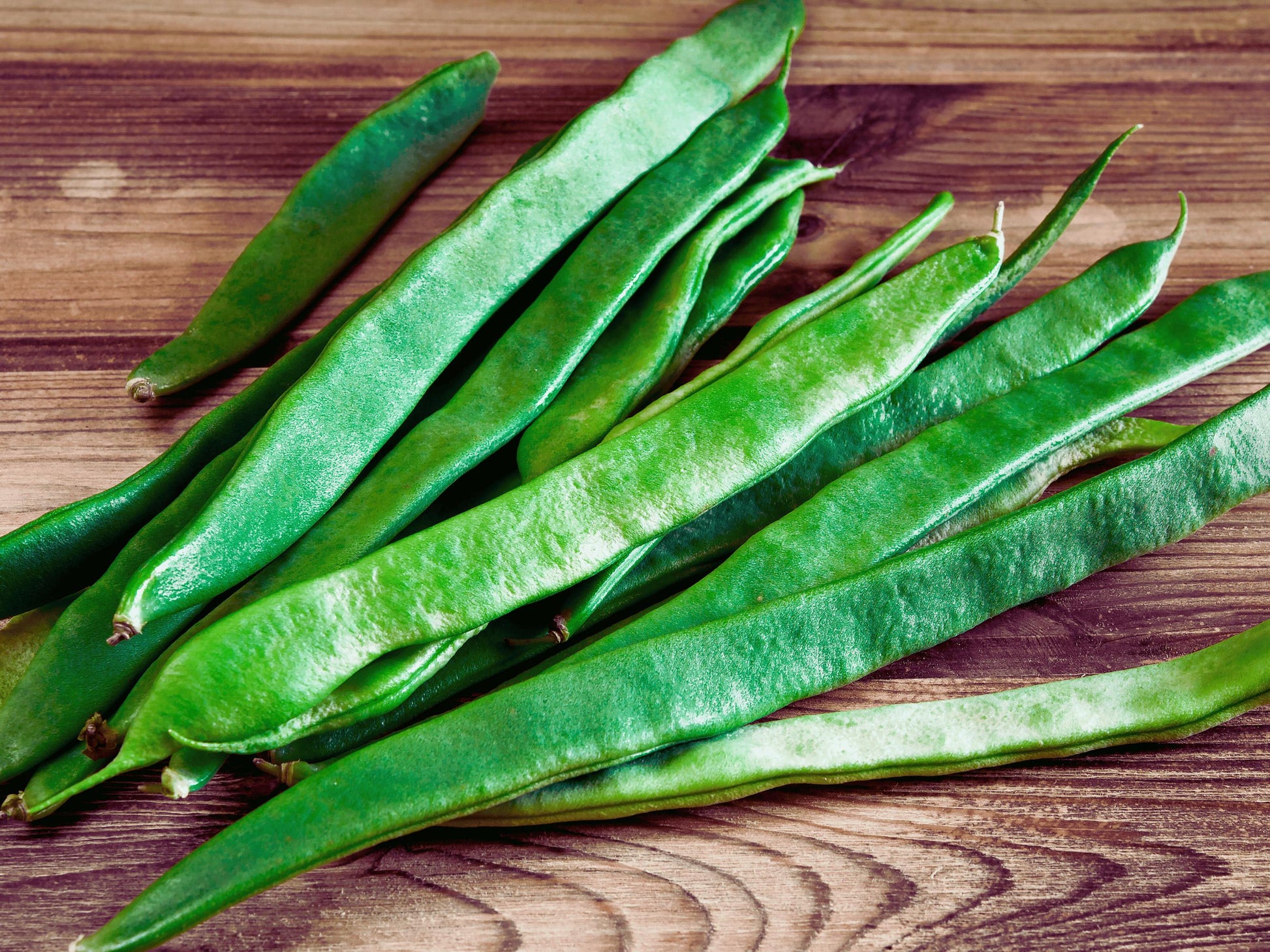 A pile of fresh green beans on a wooden surface.