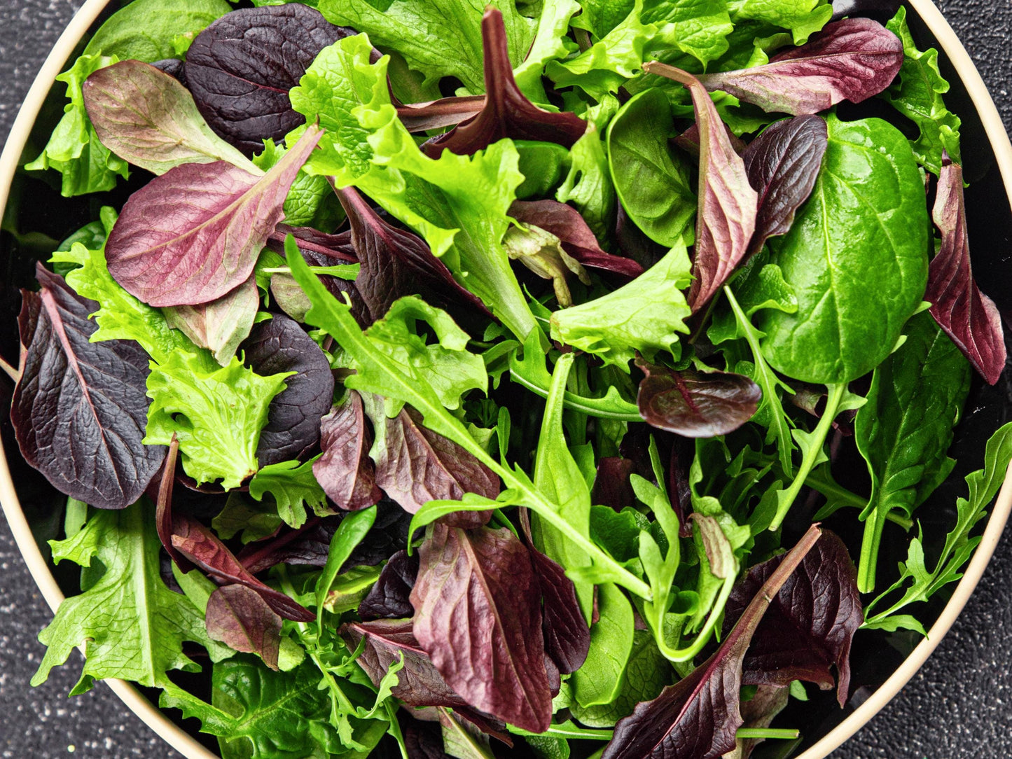 A bowl filled with a fresh salad containing various green and purple leafy vegetables.
