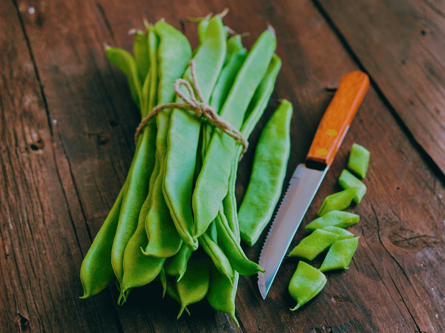A bunch of fresh green beans and a knife are placed on a wooden surface.