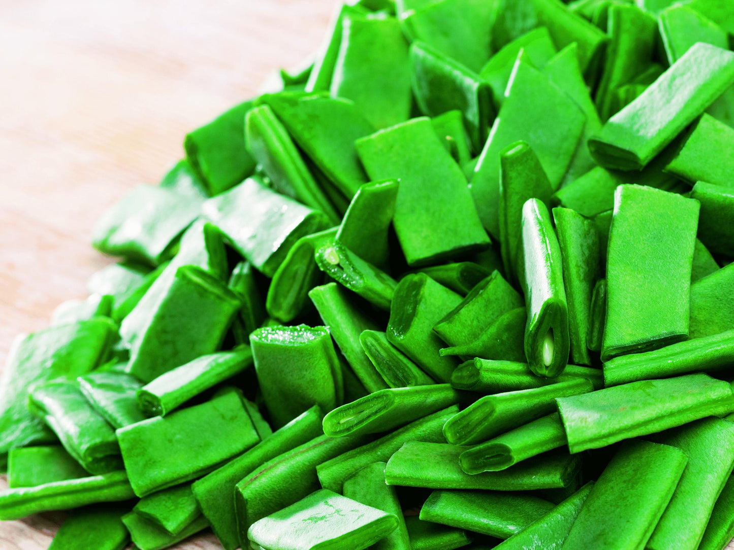 A pile of fresh green snap peas on a wooden surface.