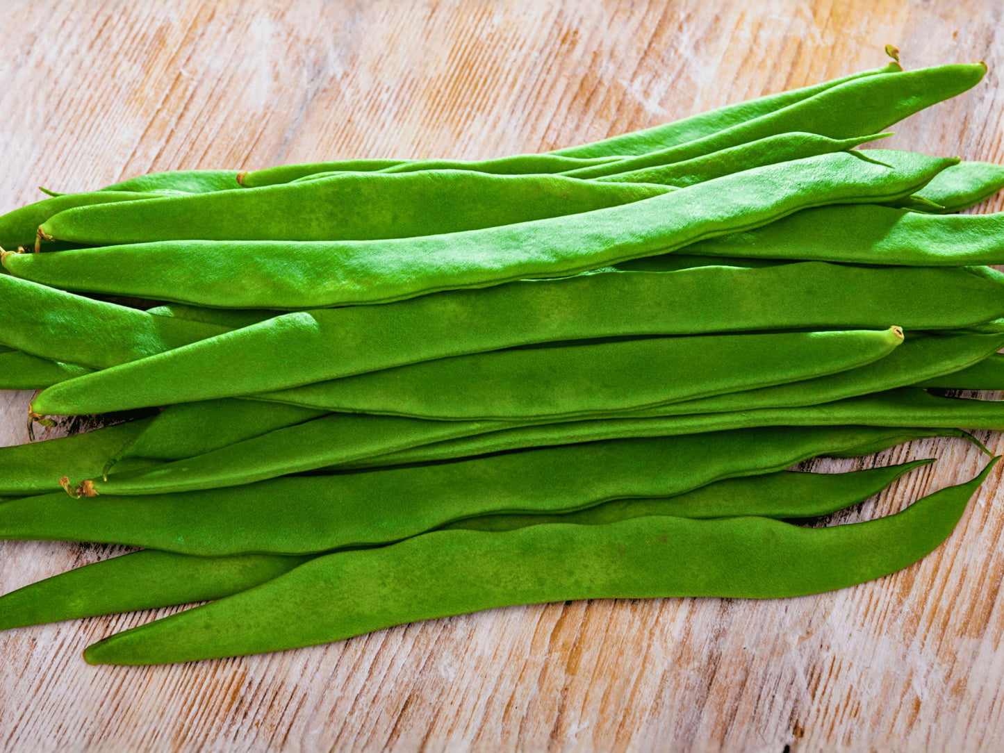 A pile of fresh green beans is neatly arranged on a wooden surface.