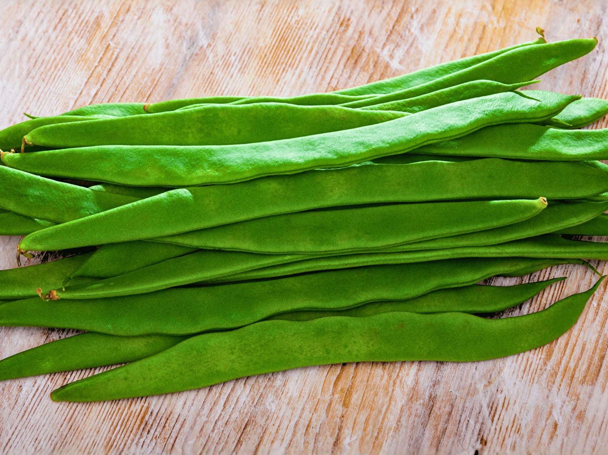 A pile of fresh green beans is neatly arranged on a wooden surface.