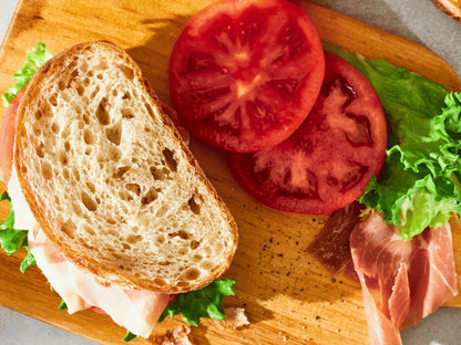 A sandwich cut in half, with fresh lettuce and tomato slices, placed on a wooden cutting board.