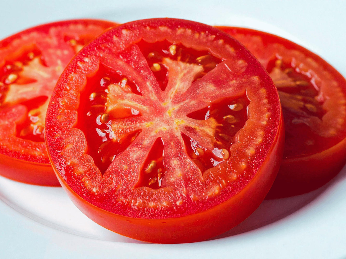 A close-up image of sliced tomatoes on a white plate.