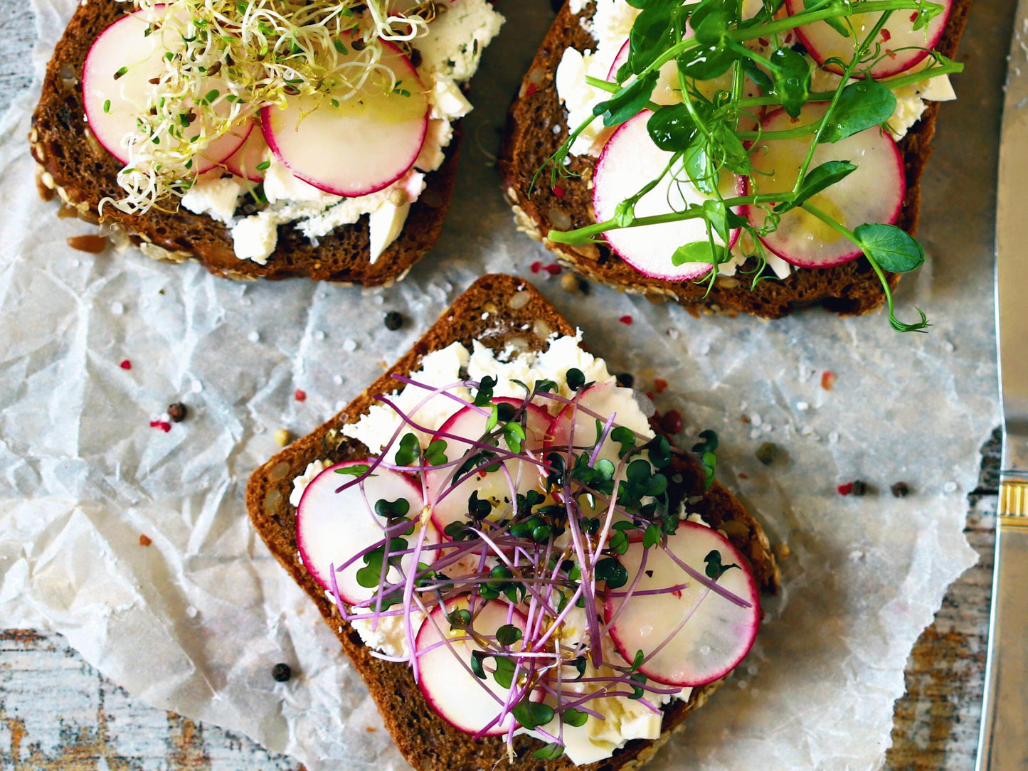 three slices of bread topped with various ingredients, including radishes, sprouts, and what appears to be cheese or cream.