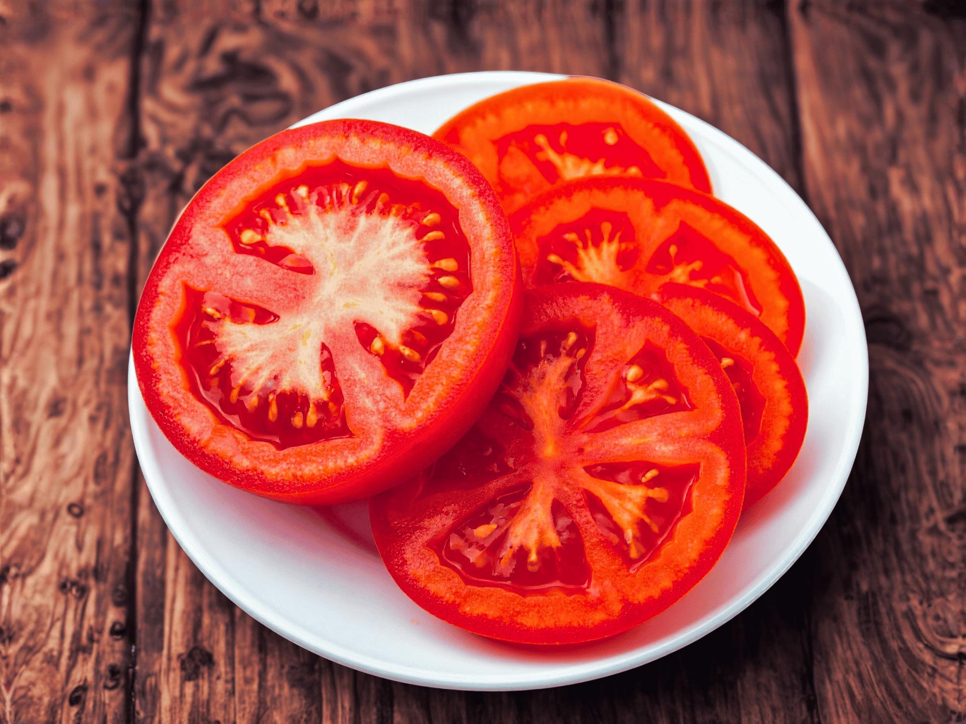 A white plate holds sliced tomatoes arranged on a wooden surface.