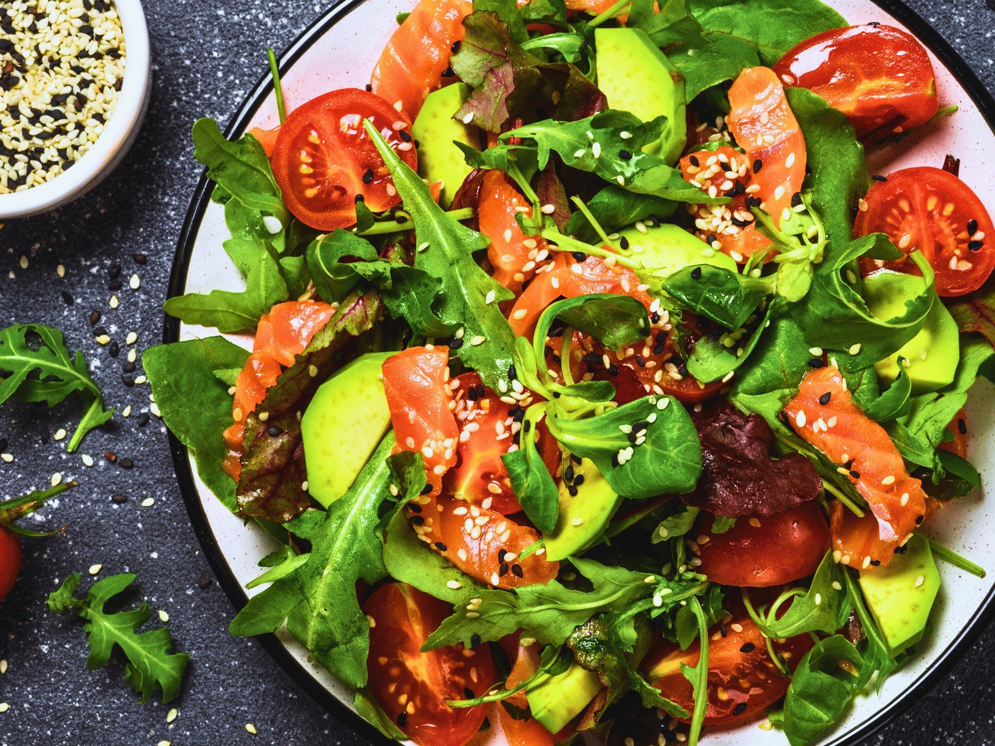A colorful salad with fresh greens, sliced tomatoes, avocado, and other vegetables, served on a plate.