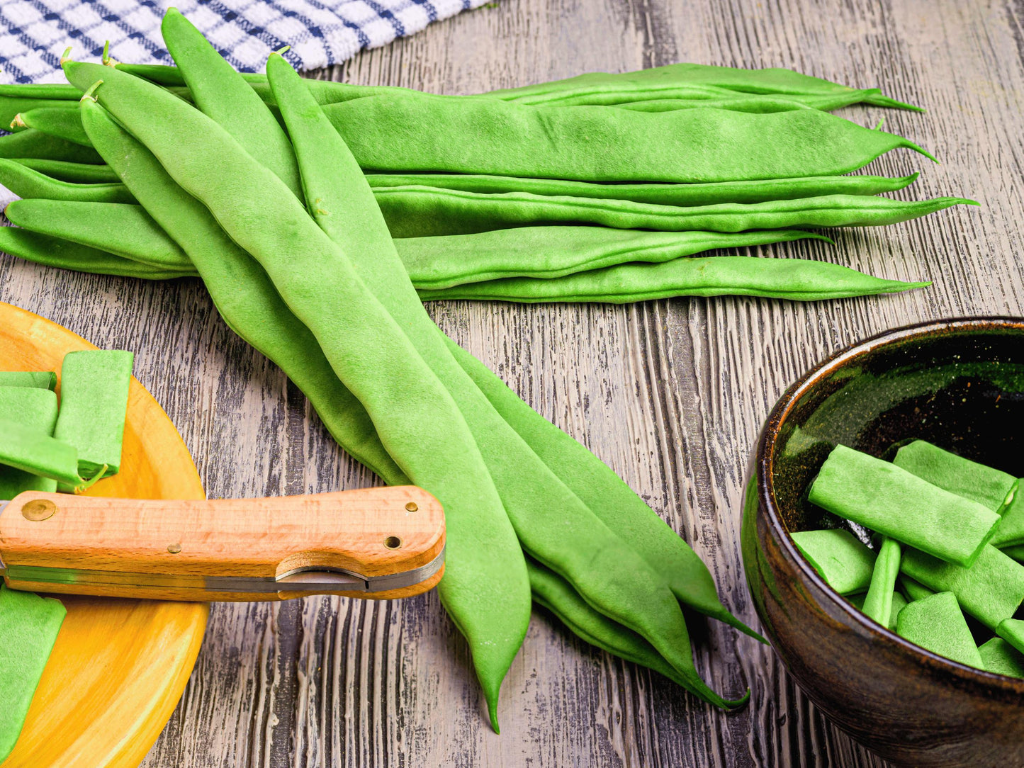 a variety of fresh green beans on a wooden surface, including whole beans and cut pieces. A knife is also visible, suggesting that the beans have been recently prepared.