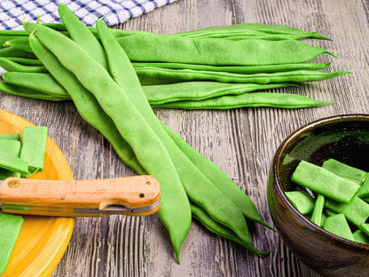 a variety of fresh green beans on a wooden surface, including whole beans and cut pieces. A knife is also visible, suggesting that the beans have been recently prepared.