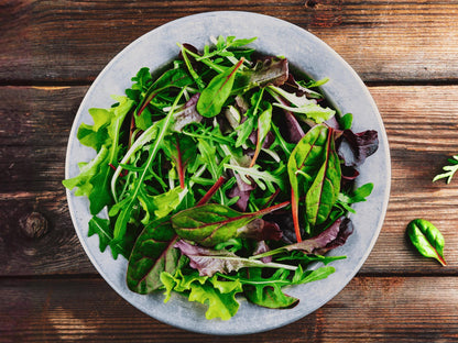 A white plate filled with a fresh salad of green and purple lettuce leaves, placed on a wooden table.
