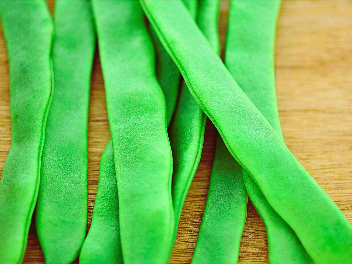A close-up image of green beans on a wooden surface.