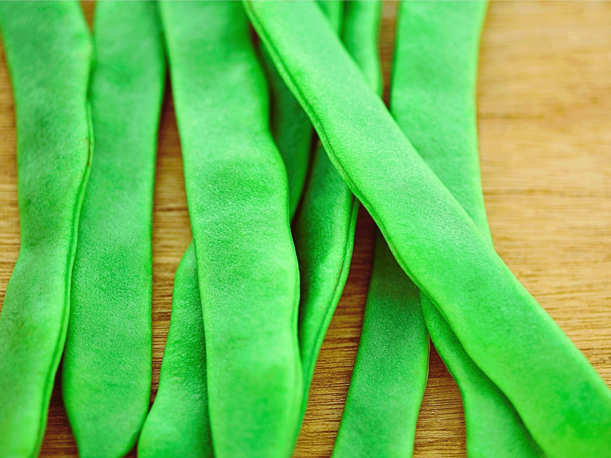 A close-up image of green beans on a wooden surface.