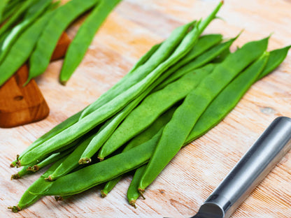 A pile of fresh green beans is displayed on a wooden surface, with a knife nearby.