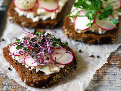 three slices of bread with various toppings, including radishes, herbs, and what appears to be cream cheese or a similar spread.