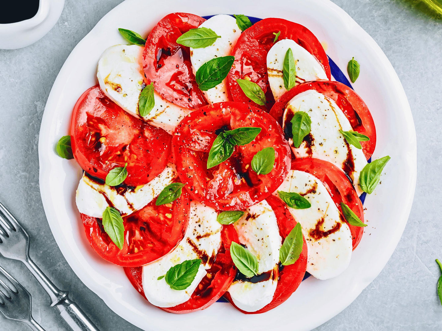 A white plate with sliced tomatoes, mozzarella cheese, and fresh basil leaves, arranged in a visually appealing manner.