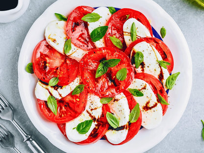 A white plate with sliced tomatoes, mozzarella cheese, and fresh basil leaves, arranged in a visually appealing manner.