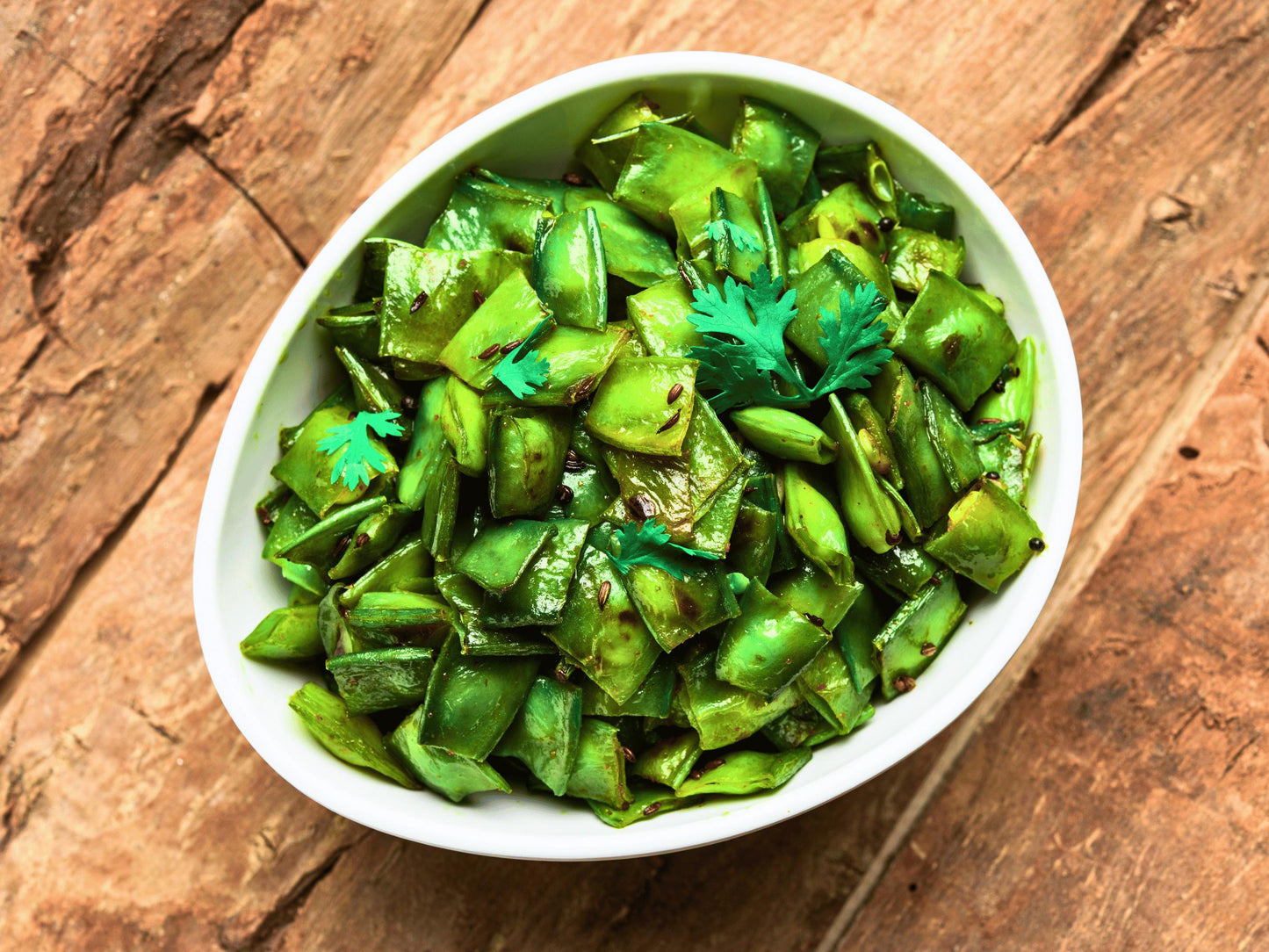 A white bowl filled with a green vegetable dish, garnished with a sprig of parsley.